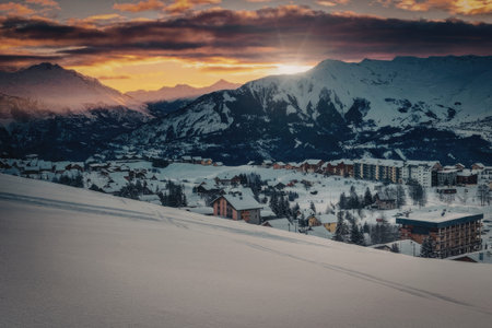 A serene snowy mountain village at sunset, with snow-covered buildings and mountains in the background.の写真素材