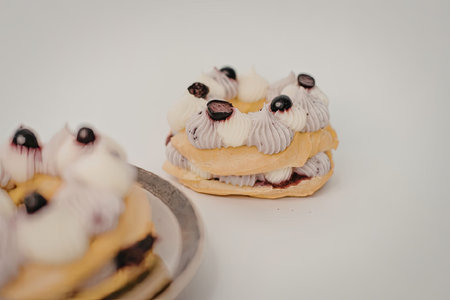 A close-up view of a pastry dessert with cream and berries on top, with another similar dessert in...