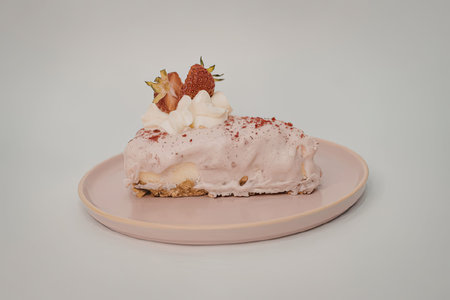 A slice of cake with pink frosting, topped with strawberries and whipped cream on a pink plate.