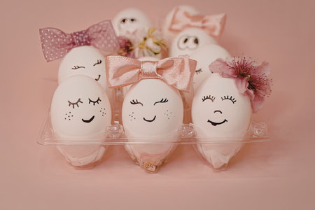 A group of eggs with smiling faces, adorned with bows and flowers, set against a pink background.