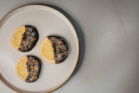 Three chocolate cookies with colorful sprinkles and lemon slices on a white plate