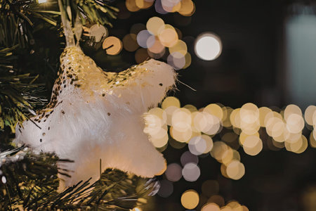 A close-up of a white angel Christmas ornament hanging on a tree with blurred lights in the...