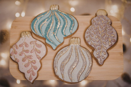 A beautifully decorated set of Christmas cookies on a wooden board with festive lights in the...