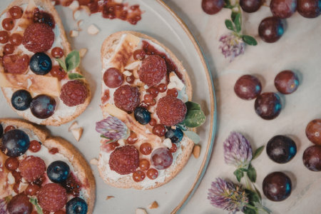 a plate of toast topped with cream, berries, and fruits, with grapes and flowers on the side