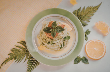A plate of green pasta with herbs and vegetables, served with a slice of orange on the side.