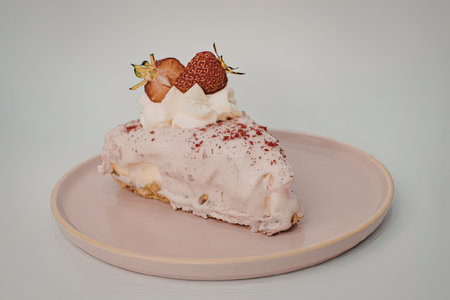 A slice of cake with pink frosting, topped with strawberries and whipped cream on a pink plate.