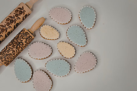 Colorful Easter egg-shaped cookies with rolling pins on a white surface