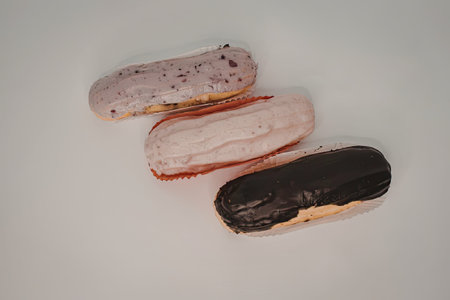 Three eclairs with different toppings, including chocolate, strawberry and cream, and purple cream.
