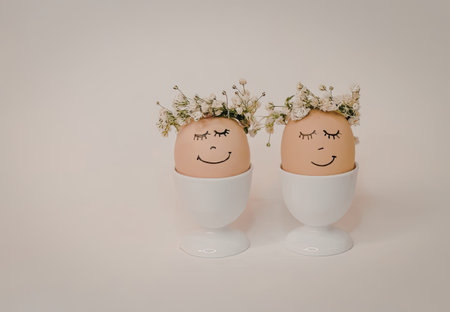 Two decorated eggs in white egg cups with floral crowns and painted faces