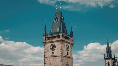 A historic clock tower with a distinctive black roof and stone walls stands under a blue sky with white clouds.の写真素材