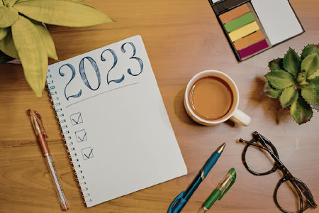 A wooden desk with a notebook, pens, coffee, glasses, and plants, representing a planning setup for...