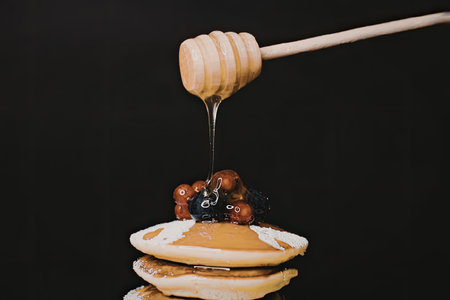 A stack of pancakes topped with berries and drizzled with honeyの写真素材