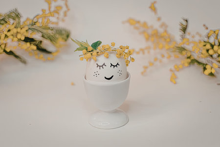 A white egg in an eggcup with a smiley face and yellow flowers on top