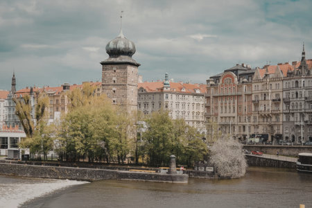 A scenic view of a city with a river in the foreground and a tower with a green dome in the...