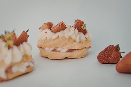 A close-up view of two cream puffs topped with strawberries and whipped cream on a white surface,...