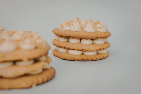 A stack of cookies with cream filling and nuts on top, placed on a plain surface.の写真素材
