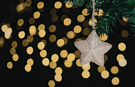 A close-up of a Christmas tree branch with a star-shaped ornament and golden bokeh lights in the background.の写真素材