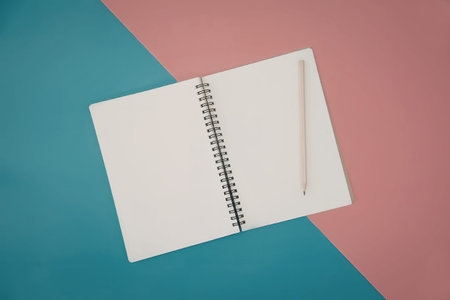 An open spiral bound notebook with a pencil on a pink and blue background