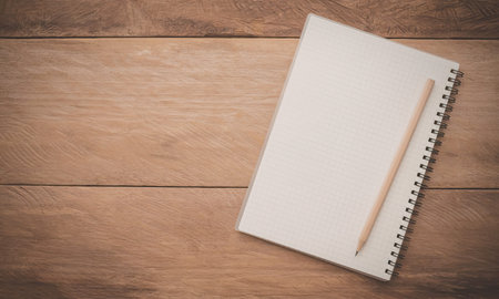 A spiral-bound notebook with a blank white page lies open on a wooden desk, accompanied by a single...