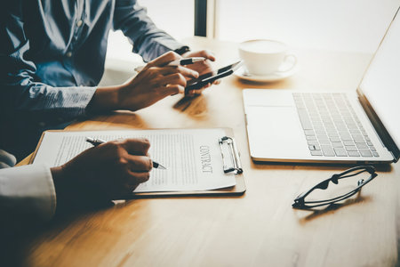 Two people sitting at a desk with a laptop, documents, and a cup of coffee, engaged in a meeting or...