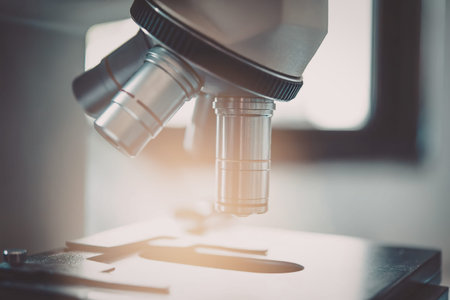 A close-up view of a microscope lens with a slide underneath, illuminated by a light source in a...