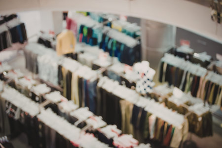 Blurry image of a clothing store with multiple racks of shirts and other clothing items on display.