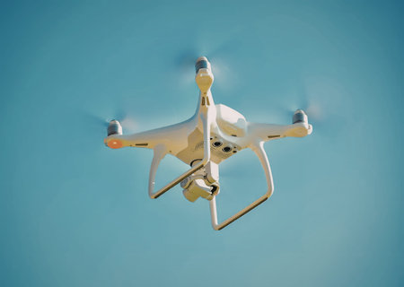 A white drone flying in a clear blue sky with its propellers spinning.