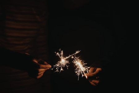 A pair of hands holding sparklers in a dark environment, sparklers lit up brightly.