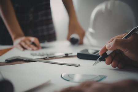 Close-up of hands working on architectural plans with drafting tools on a table.