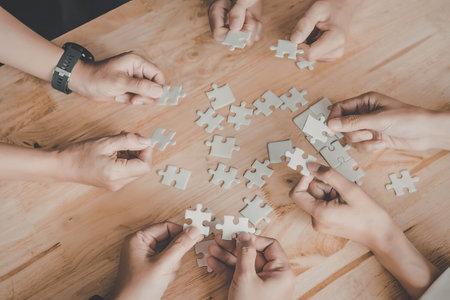 Multiple hands working together on a puzzle on a wooden table.