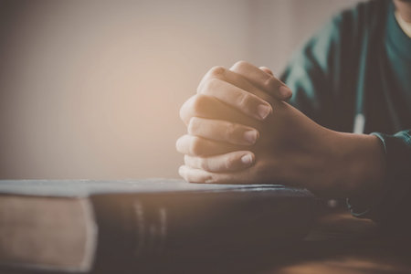 A person wearing a green shirt has their hands clasped together in prayer on top of a book,...