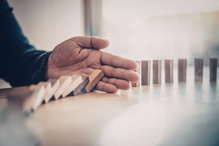 A person's hand stopping a row of falling dominoes, conveying prevention or protection.