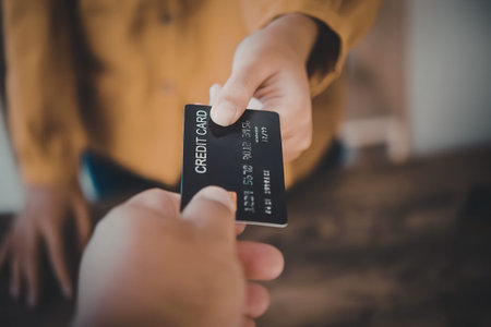 A close-up shot of two hands, one handing a black debit card to the other, with the person in the...