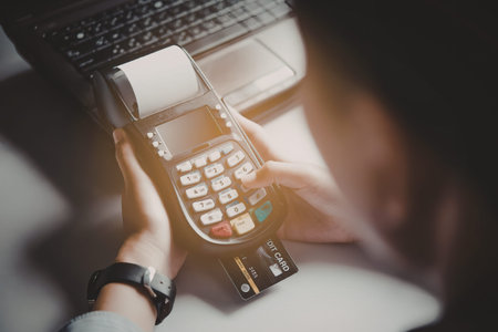 A person is shown holding a payment terminal and a credit card, with a laptop in the background.