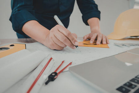 A person in a blue shirt working on architectural plans with a ruler and pen.