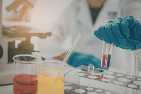 A scientist in a lab coat and blue gloves working with test tubes and beakers in a laboratory...