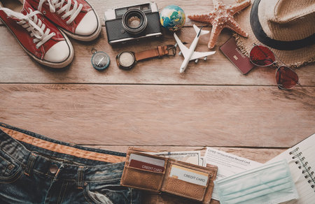 A collection of travel essentials such as a camera, shoes, starfish, globe, and passport on a wooden...