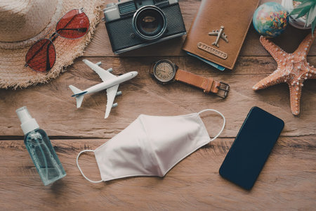 A collection of travel essentials including a face mask, hand sanitizer, and a smartphone, arranged...