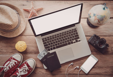 A laptop surrounded by travel-related items on a wooden table.
