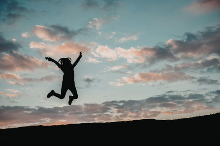 A person jumping in the air with arms outstretched against a backdrop of a vibrant sunset sky with...