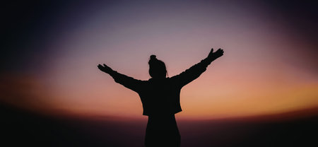 A person standing with arms outstretched in silhouette against a vibrant sunset background