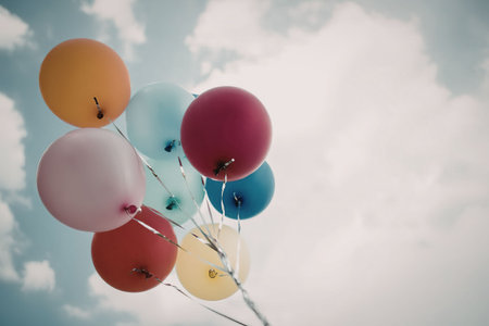 A cluster of colorful balloons soaring against a bright blue sky with fluffy white clouds.