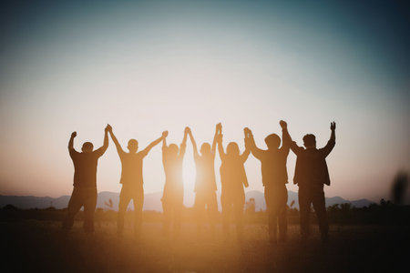A group of people standing on a hill with their arms raised at sunset