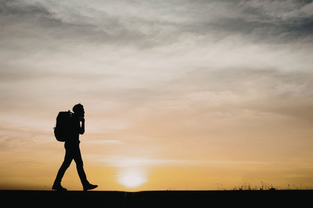 A silhouette of a man walking towards the sunset with a backpack on his back.