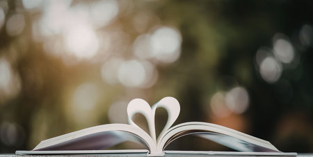 An open book with pages folded into a heart shape sitting on a table with a blurry green background.