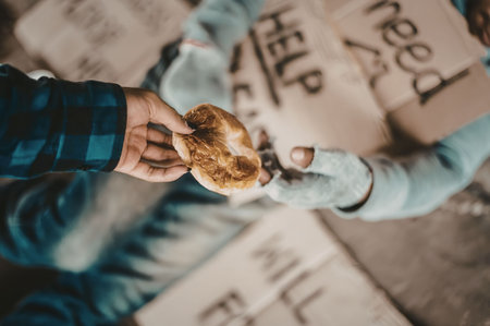 A person giving a donut to a homeless individual who is holding a cardboard sign on the street.の写真素材