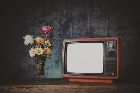 A vintage red television set with a blank screen sits next to a vase of colorful flowers on a wooden...
