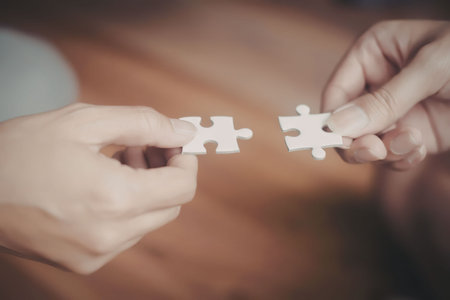 Two hands, presumably belonging to different individuals, are shown holding puzzle pieces that fit...