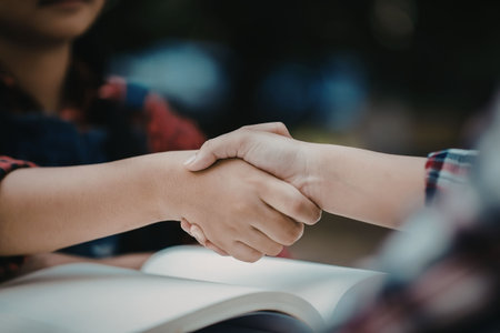 Close-up of two people shaking hands over an open book, possibly a student and teacher or two...