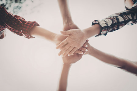 Four people stacking their hands on top of each other in a symbol of unity and teamwork.